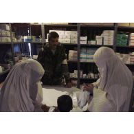 Consultations pour la population civile à l'hôpital jordanien de l'aéroport de Mazar e Charif. Femmes afghanes voilées venues consulter avec un enfant, au comptoir de la pharmacie, où un militaire jordanien leur a remis un sac contenant des médicaments.