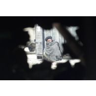 A Mazar e Charif, vue à travers un trou d'éclat d'obus d'un Afghan s'abritant du froid adossé contre une caisse.