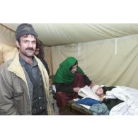 Activités de l'hôpital jordanien de Mazar e Charif. Service d'hospitalisation d'enfants malades ou blessés. Une femme se tient au chevet de son enfant qui porte un bandage sur la tête, sous le regard d'un parent.