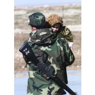 Activités de l'hôpital jordanien de Mazar e Charif. Un militaire jordanien, son fusil dans le dos, porte un enfant dans ses bras.