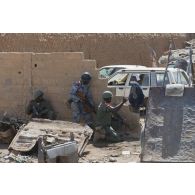 Des soldats et des gendarmes maliens progressent à couvert d'un mur dans une rue de Gao, au Mali.