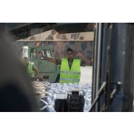 Un technicien logistique guide le transport d'une palette de bouteilles d'eau par un engin de levage sur la base aérienne (BA) 367 Capitaine françois Massé à Cayenne, en Guyane française.