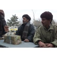 Marchands pratiquant le change au marché de l'argent du centre-ville de Mazar e Charif, veillant sur des paquets de liasses de billets en afghani, la monnaie locale.