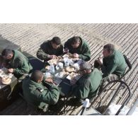 Dernier déjeuner en plein air des derniers militaires du détachement français présents à l'aéroport de Mazar e Charif avec des plateaux repas et sur des caisses de matériel constituant des sièges de fortune. Table de convives.