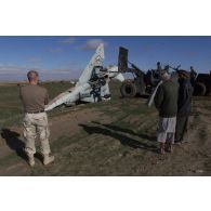 Pour préparer l'installation d'un nouveau camp, les démineurs américains poussent les épaves des anciens avions de combat MIG de l'armée soviétique à l'aide d'un engin du génie en dehors de la piste de l'aéroport de Mazar e Charif, sous le regard d'Afghans.