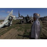 Pour préparer l'installation d'un nouveau camp, les démineurs américains poussent les épaves des anciens avions de combat MIG de l'armée soviétique à l'aide d'un engin du génie en dehors de la piste de l'aéroport de Mazar e Charif, sous le regard d'Afghans.