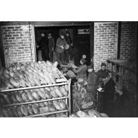 Des soldats rangent des boules de pains dans de vastes paniers métalliques.