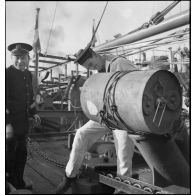 Un matelot arrime une grenade sous-marine sur le berceau d'un lance-grenades à bord du chalutier armé en patrouilleur La Lorientaise.
