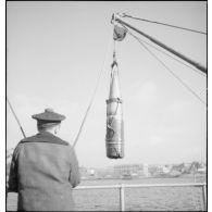 Un marin manipule un obus de 330 mm suspendu à un palan à bord du cuirassé Dunkerque.