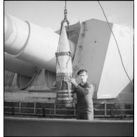 Un marin manipule un obus de 330 mm suspendu à un palan devant une des tourelles quadruples du cuirassé Dunkerque.