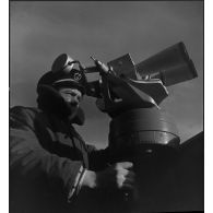 Un officier marinier assure une veille sur le cuirassé Dunkerque ou Strasbourg à l'aide de jumelles de surveillance.