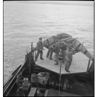 Chargement d'un canon de 75 mm sur la plage avant d'un chalutier réquisitionné et armé par la Marine nationale pour servir de dragueur de mines.