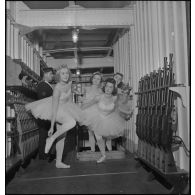 Des danseuses d'un corps de ballet traversent l'armurerie du porte-avions Béarn à bord duquel elles participent à un spectacle pour la soirée, la veille de Noël.