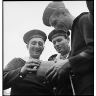 Des membres d'équipage du contre-torpilleur Le Malin examinent une bouée endommagée par une munition de mitrailleuse d'avion.