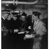 L'aumônier du cuirassé Dunkerque en tenue d'alerte s'entretient avec des médecins et infirmier du bord.