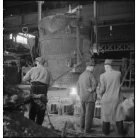 A l'intérieur de l'usine des ouvriers travaillent devant un fourneau.