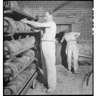 Des boulangers militaires sortent des pains du four et les rangent sur des étagères.