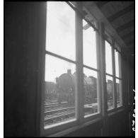 En gare de Trappes une locomotive est photographiée au travers de la fenêtre d'un baraquement.