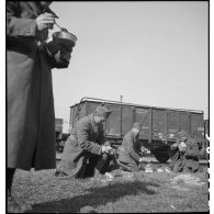 Photographie de groupe de soldats qui mangent assis près d'une voie ferrée en gare de Trappes.