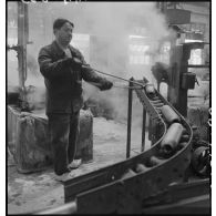 Un ouvrier se sert d'une pince pour saisir un corps d'obus.