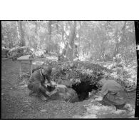 Deux soldats s'affairent près d'un trou de combat dans un sous-bois.