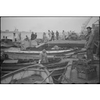 Des marins, de corvée de vivres, embarquent dans des chaloupes le ravitaillement destiné à une escadre qui mouille au large.