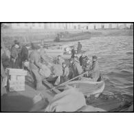 Des marins, de corvée de vivres, embarquent dans des chaloupes le ravitaillement destiné à l'escadre qui mouille au large.