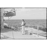 Un marin est de quart sur le pont du croiseur léger la Marseillaise. Il porte sur le dos un masque à gaz AFM 34.