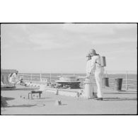 Des marins assurent une maintenance sur les chaînes d'ancrage sur le pont avant du croiseur léger la Marseillaise. Ils portent sur le dos un masque à gaz AFM 34.