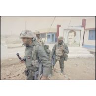 Deux radios du 3e RIMa (régiment d'infanterie de marine), émetteur-récepteur TRPP-13 au dos, se tiennent devant un portrait de Saddam Hussein à Al Salman, alors que deux officiers, dont un lieutenant se concertent. Les marsouins portent leur équipement individuel, un S-3P (survêtement de protection à port permanent) NBC (risque nucléaire, bactériologique et chimique) et leur fusil d'assaut FAMAS.