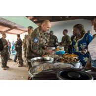 Le général de brigade Éric Bellot des Minières déguste un mets local lors du repas donné en clôture de la cérémonie de réouverture du marché de Bambari.