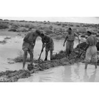 Armés de pelles, les hommes tentent de créer des digues pour limiter l'inondation de leur camp par les eaux de pluie.