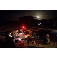 Des soldats prennent leur repas à la lueur de leur lampe frontale lors de la halte nocturne d'un convoi sur l'axe Berliet, au Niger.