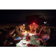 Des soldats prennent leur repas à la lueur de leur lampe frontale lors de la halte nocturne d'un convoi sur l'axe Berliet, au Niger.