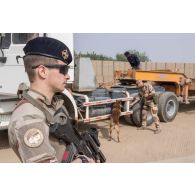 Un fusilier commando de l'air sécurise une zone de chantier pendant d'un maître-chien inspecte un camion semi-remorque d'une entreprise civile sur la base aérienne de N'Djamena, au Tchad.