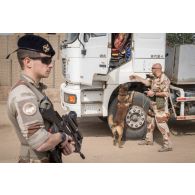 Un fusilier commando de l'air sécurise une zone de chantier pendant d'un maître-chien inspecte un camion semi-remorque d'une entreprise civile sur la base aérienne de N'Djamena, au Tchad.