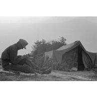 Un membre d'équipage d'un blindé Panzer III (non visible) fait des travaux de réparation près de sa tente en partie camouflée.