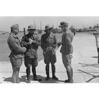 Sur le port, deux officiers allemands discuttent avec des policiers italiens de la PAI (Polizia dell'Africa italian).