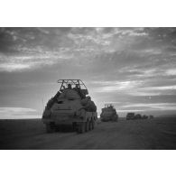 Un blindé SdKfz-263 roule dans le désert au crépuscule au milieu d'une colonne de véhicules.