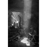 Deux soldats utilisent un téléphone de campagne dans la grotte sous un rayon de lumière. L'un d'eux fume.