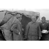 Trois officiers italiens près d'un véhicule recouvert d'une bâche et de ponchos.