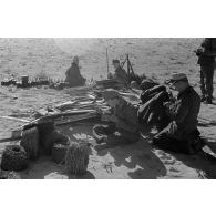 Des soldats mangent près de faisceaux de fusils Kar-98k, de mines antipersonnel, de rouleaux de fils barbelés.