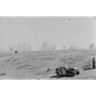Une voiture Kübelwagen immobile, deux soldats viennent de disposer un poste radio et son antenne, au loin, la poussière provoquée par des explosions.