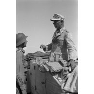Le colonel (Oberst) Alfred Bruer commandant du Panzer-Artillerie-Regiment 155 de la 21. Panzer-Division, debout dans une voiture Kübelwagen, parle avec ses officiers.