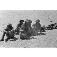 Des prisonniers britanniques accroupis et allongés dans le sable.