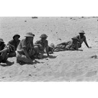 Des prisonniers britanniques accroupis et allongés dans le sable.