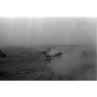 Une colonne de véhicules progresse dans le désert en produisant d'importants nuages de poussière.