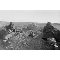 Un groupe de soldats allongés sur le sol observe le terrain. Tir de fusées dans le lointain.