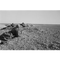 Un groupe de soldats allongés sur le sol observe le terrain. Tir de fusées dans le lointain.