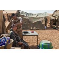 Un soldat se fait couper les cheveux par son camarade en zone vie du camp de Gao, au Mali.